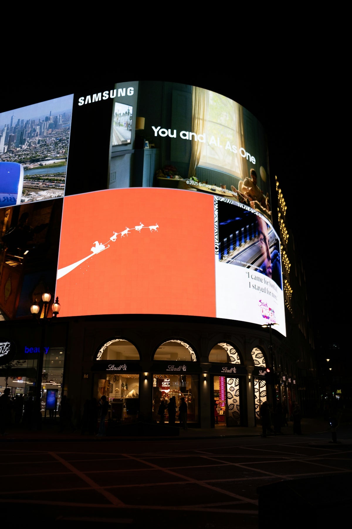Bright digital billboards illuminate a city corner at night.