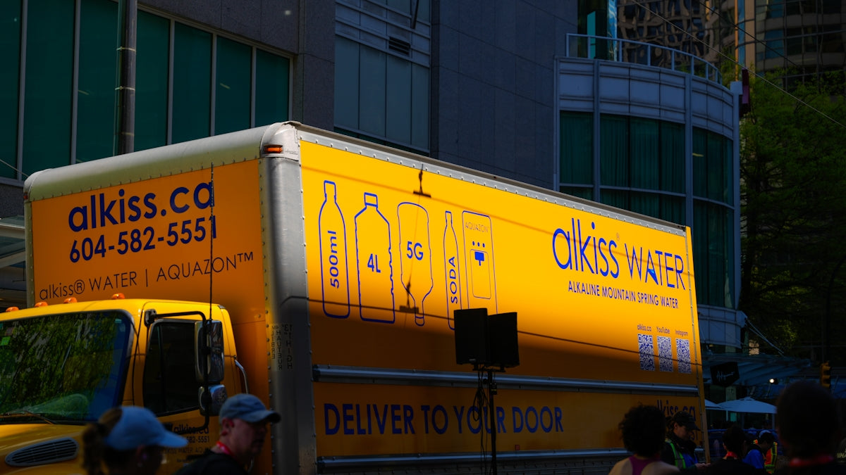 Yellow delivery truck with alkiss water branding.