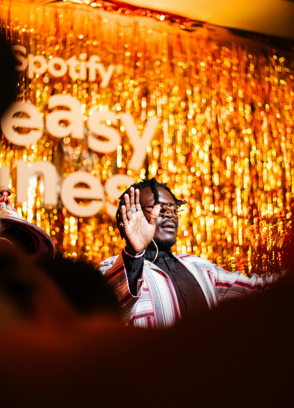 Man on stage with raised hand against golden spotify backdrop