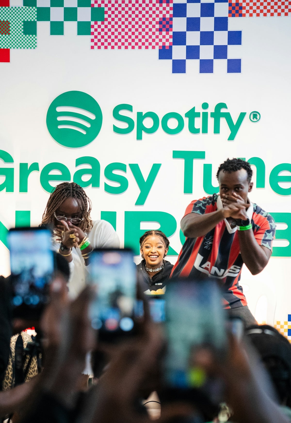 Three people posing for a crowd of smartphones in front of a Spotify backdrop